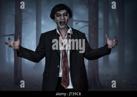 Effrayant zombie asiatique homme portant costume avec main ouverte sur la forêt sombre Banque D'Images