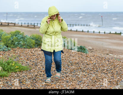 Personnes âgées / femme d'âge moyen sur une plage par un froid jour de vent au Royaume-Uni. Banque D'Images