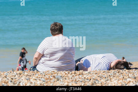L'excès de femme assise sur une plage. Grande dame était assis au soleil sur une plage dans le Royaume-Uni. Personne obèse sur une plage. Banque D'Images