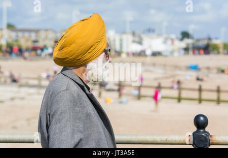 Homme sikh portant un turban debout à la côte à la recherche à la plage dans le sud de l'Angleterre, Royaume-Uni. Banque D'Images