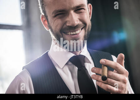 Close-up portrait of handsome smiling homme confiant de fumer un cigare à l'intérieur Banque D'Images