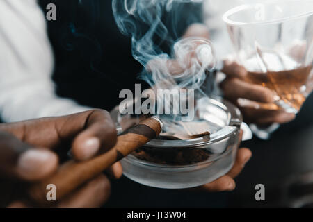 L'équipe d'entreprises multiculturelles passer du temps, fumer un cigare et boire du whisky Banque D'Images