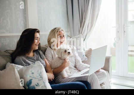 Mère et sa fille quelqu'un appel vidéo sur leur ordinateur portable. Ils sont souriants et forme à l'écran. Son chien est assis avec eux. Banque D'Images