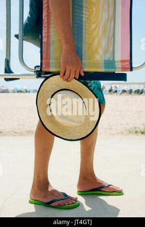 Libre d'un jeune homme de race blanche portant une chaise de plage et un chapeau de paille à la main, en allant ou en revenant de la plage Banque D'Images