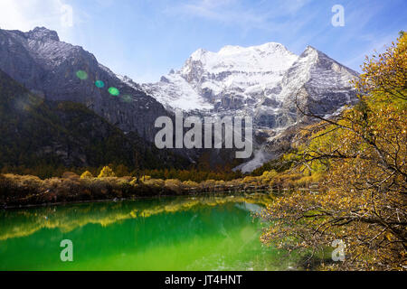 Shangri La, le vert de couleur claire Pearl Lake avec la sainte montagne enneigées Chenresig et jaune orangée dans les arbres d'automne dans la vallée national Yading Banque D'Images