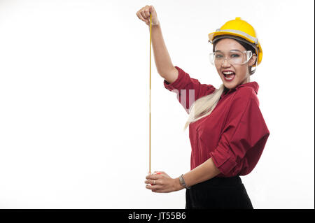 Asian Woman Engineer porter des casques et lunettes de sécurité jouant avec ruban de mesure dans ses mains. L'ingénierie et de l'occupation industrielle concept Banque D'Images