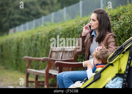 Occupé à l'aide de téléphone mobile avec mère enfant assis dans la PRAM. Banque D'Images
