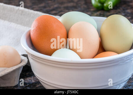 Photo horizontale multicolore d'oeufs dans un bol blanc et certains dans le carton sur le côté sur un comptoir de cuisine avec un poivron vert en arrière-plan Banque D'Images