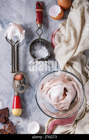 Ingrédients et ustensiles pour la cuisson de la meringue. Les blancs d'oeufs fouettés, le sucre en poudre, oeufs cassés, vintage et tamis mélangeur de main sur lin gris serviette sur te Banque D'Images