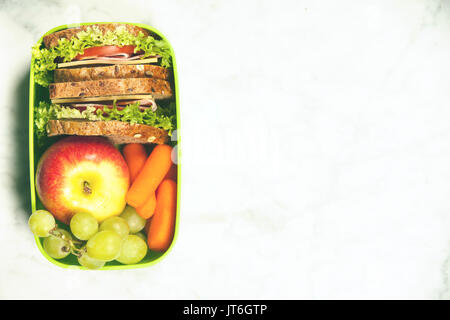 L'école verte boîte à lunch avec sandwich, pomme, raisin et carotte close up sur fond blanc. De saines habitudes alimentaires concept. Banque D'Images