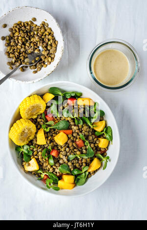 Salade de lentilles aux herbes, les tomates et les pêches dans un bol blanc est photographié en vue de dessus. Il est accompagné par des lentilles cuites dans un bol et tahini Banque D'Images