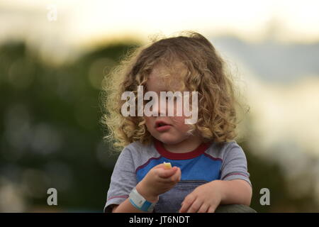 Une jeune fille aux cheveux bouclés de manger à l'extérieur. Banque D'Images