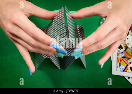 Femme mains assemblage château de cartes. Feutre vert contre l'arrière-plan avec cartes et jetons de poker. Casino Jeu et thème Banque D'Images