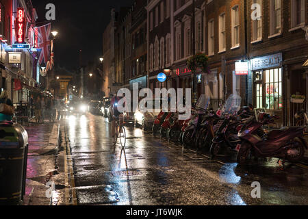 Vue d'une rangée de cyclomoteurs et un cycliste sur Dean Street à Soho à Londres sur une nuit pluvieuse. À partir d'une série de photos prises sur une nuit pluvieuse à Soho, Lon Banque D'Images