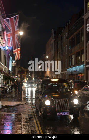 Vue d'un taxi taxi noir de Londres (avec drapeaux Union Jack) sur Dean Street à Soho, Londres. À partir d'une série de photos prises sur une nuit pluvieuse à Soho, Lond Banque D'Images