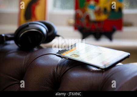 Londres, Royaume-Uni. Samsung smartphone avec paire d'écouteurs de bras assis sur un fauteuil en cuir luxueux. Banque D'Images