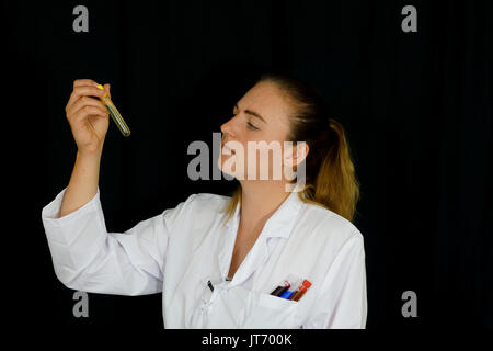 Une jeune femme examine des tubes à essai remplis de liquides colorés sur fond noir. Banque D'Images