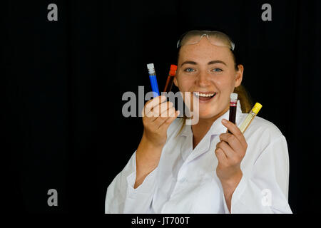 Une jeune femme examine des tubes à essai remplis de liquides colorés sur fond noir. Banque D'Images