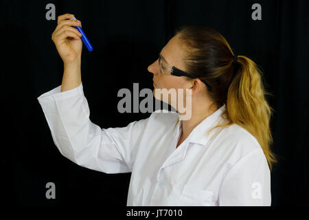 Une jeune femme examine des tubes à essai remplis de liquides colorés sur fond noir. Banque D'Images