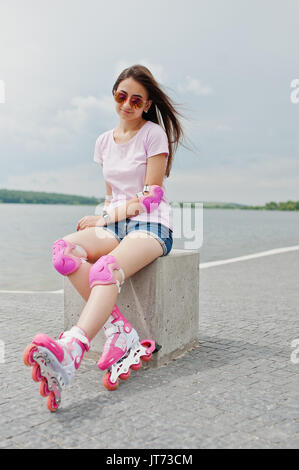 Portrait d'une jolie jeune femme en short, t-shirt, lunettes de soleil et de rollers assis sur le banc en béton dans la piscine patinoire roller Banque D'Images