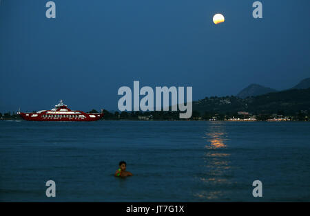 La pleine lune avec une éclipse partielle, s'élève alors qu'un jeune garçon cools off dans la mer dans la baie d'Oropos en Eubée, à 30 milles à l'est d'Athènes, Grèce. Lundi 07 Banque D'Images