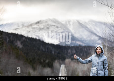 Jeune femme solitaire de l'auto-stop sur une route d'hiver avec de belles montagnes enneigées en arrière-plan Banque D'Images