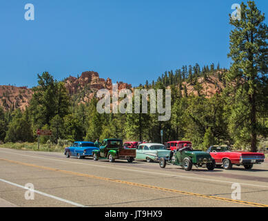 Groupe de vieilles voitures en stationnement sur la route près de Red Canyon, Utah ; montagnes en arrière-plan Banque D'Images