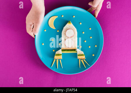 Personne tenant funny salle de petit-déjeuner colorée pour enfant en forme de fusée avec lune et étoiles sur plaque bleue isolé sur pink Banque D'Images