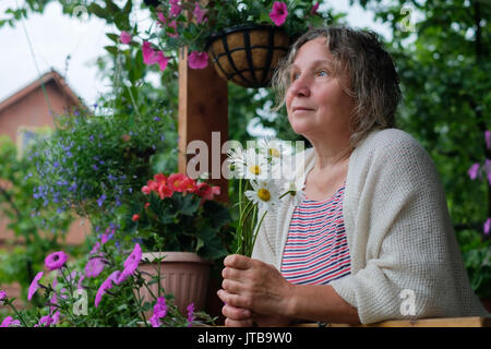 Senior woman in green garden avec des fleurs dans les mains Banque D'Images