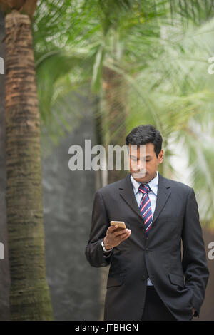 L'homme d'affaires indien à l'aide de son téléphone intelligent à l'extérieur, dans la ville d'Asie. Banque D'Images