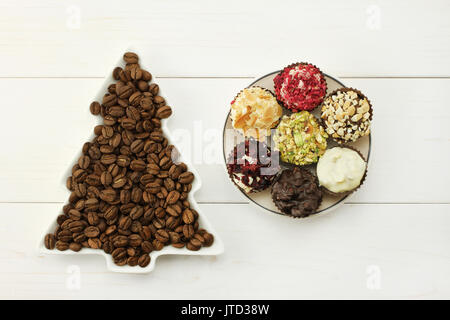 Les grains de café torréfié en blanc lave-spruce, ensemble de chocolats en soucoupe ronde blanche sur fond de bois blanc Banque D'Images