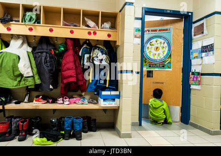 Un enfant assis à l'extérieur d'une salle de classe dans une école, enlever ses bottes et son manteau d'hiver, se préparer à commencer la journée d'école, Canada Banque D'Images