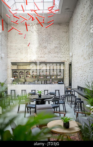 Un bar élégant avec des murs texturés et une grande fenêtre au plafond. Il y a des tables rondes en bois, tabourets et chaises, un grand nombre de plantes, sol carrelé dégrillage Banque D'Images