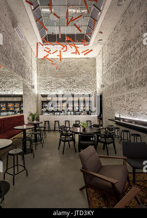 Bar lumineux avec murs texturés et une grande fenêtre au plafond. Il y a des canapés, tables rondes noir, tabourets et chaises, plantes, sol carrelé bar r Banque D'Images