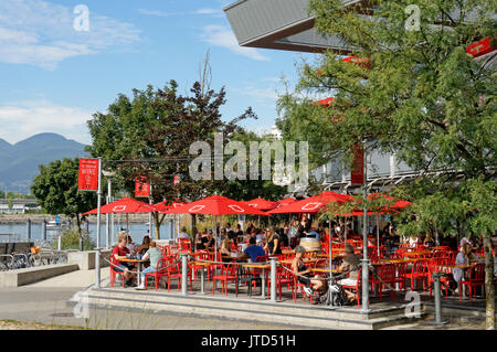 Des gens assis sur le bord de l'eau du robinet, un patio extérieur et le canon restaurant dans le village olympique, le False Creek, Vancouver, BC, Canada Banque D'Images