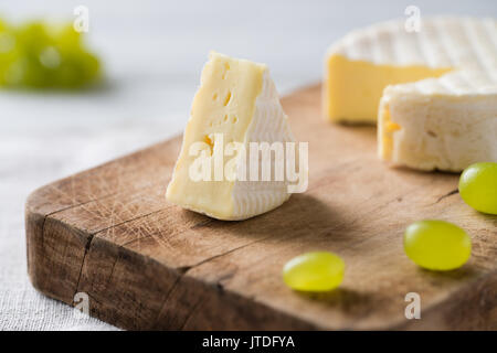 Gros plan du fromage français de Normandie en tranches avec raisins vert sur une planche en bois sur fond blanc Banque D'Images