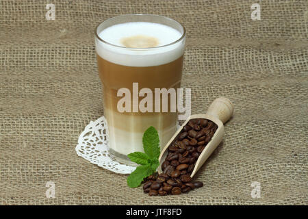Latte Macchiato en verre avec des grains de café sur fond brun Banque D'Images