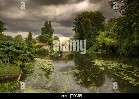 Historique anglais pont médiéval dominant la rivière Avon à côté le château de Warwick avec feuillage vert luxuriant et sauvage de l'été les nuages de tempête. Banque D'Images