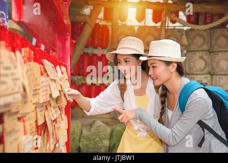 Les voyageurs à la recherche des amies souriant à prier et plaques en bois du geste de pointage montrant lors d'un voyage au Japon temple bouddhiste. Banque D'Images
