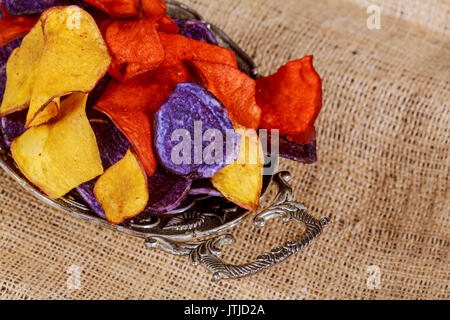 Blue chips de pommes de terre et Betteraves rouges Carottes croustilles salées dans le sac de l'arrière-plan en bois. Banque D'Images