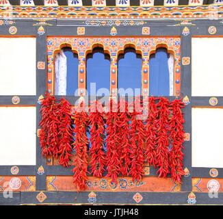 Red Chili piment sec par pendaison en face de Bhoutanais traditionnel en bois peint de couleur fenêtre, Bhoutan Banque D'Images