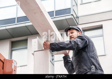 Un homme fort builder à l'obscurité dans une combinaison et un plafond de la construction construit une maison d'été sur la rue de les poutres en bois peint en blanc, sur la b Banque D'Images