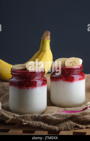 Garni de yogourt et petits fruits banane sur tissu de jute. Fond noir. Banque D'Images