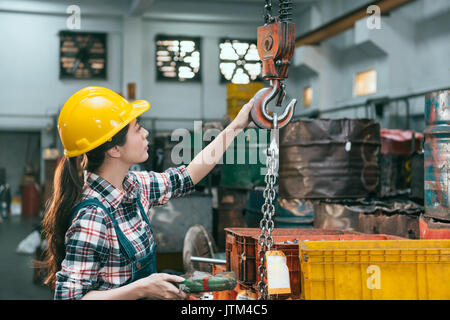 Belle jeune femme qui travaille en usine de l'industrie de la chaîne de réglage usinage grues quand elle prête à tour de transport des produits finis. Banque D'Images