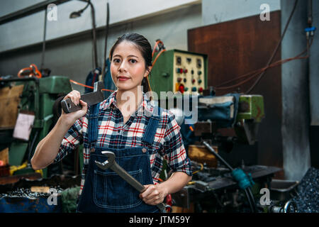 Jeune femme en usine industrielle tenant deux clés grande confiance smiling face à l'appareil photo dans l'article machine-usine. Banque D'Images