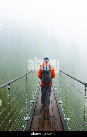 Un homme marche sur un pont suspendu sur un jour d'automne pluvieux à Squamish, en Colombie-Britannique. Banque D'Images