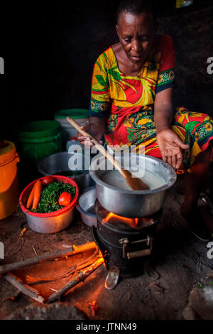 Chez elle, près d'Arusha, en Tanzanie, Julieth Mollel, sœur de Solar, prépare un dîner d'ugali, de légumes et de haricots sur sa cuisinière propre. L'ugali est un aliment de base consommé dans de nombreux pays d'Afrique et est de la bouillie de farine de maïs. travailler dans sa cuisine extérieure compacte la nuit est plus facile maintenant avec la cuisinière propre qui émet très peu de fumée et utilise seulement une fraction du bois de chauffage d'une cuisinière traditionnelle à trois pierres. Banque D'Images