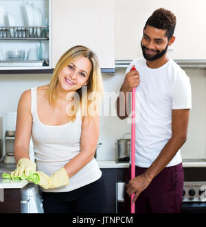 Mari Noir avec blanc smiling young woman dusting dans cuisine domestique Banque D'Images