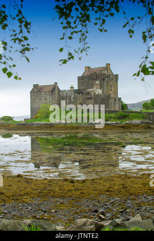 Vue sur la spectaculaire château Eilean Donan reflétée dans l'eau peu profonde du lac contre le ciel bleu en Ecosse Banque D'Images