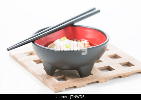 Wonton soup servi dans un bol noir sur un sous-plat en bois. Banque D'Images